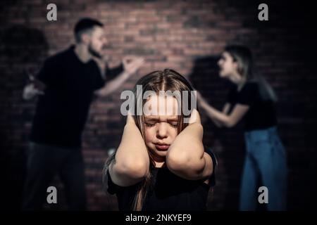 Piccola ragazza spaventata e vista offuscata dei genitori in lite sullo sfondo. Violenza domestica Foto Stock