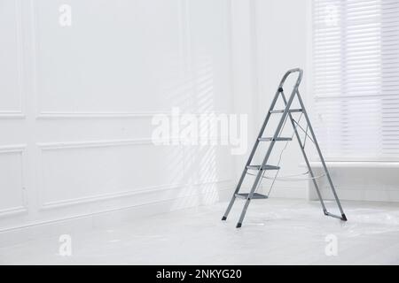 Scala a cavalletto in metallo su pavimento coperto di plastica in camera vuota, spazio per testo Foto Stock