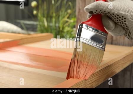 Lavoratore che applica vernice corallo su superficie di legno contro sfondo sfocato, primo piano. Spazio per il testo Foto Stock