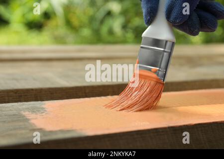 Lavoratore dipingere superficie in legno con colorante corallo all'aperto, primo piano. Spazio per il testo Foto Stock