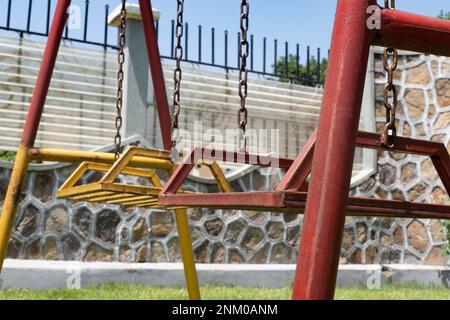 Altalena per bambini vecchi e arrugginiti. Verniciato di colore rosso e giallo. Parco giochi per bambini. Foto Stock