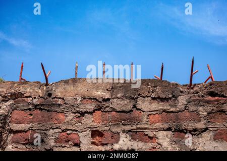 Muro di mattoni rossi con punte affilate sulla parte superiore. Cielo blu chiaro con nuvole. Tema della prigione e della libertà. Foto Stock