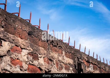 Muro di mattoni rossi con punte affilate sulla parte superiore. Cielo blu chiaro con nuvole. Tema della prigione e della libertà. Foto Stock