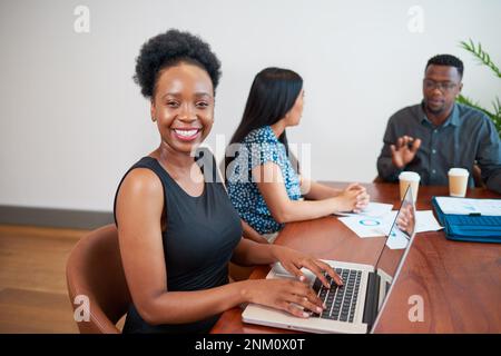 Giovane donna nera che digita sul computer portatile durante una riunione con i colleghi nella sala riunioni Foto Stock