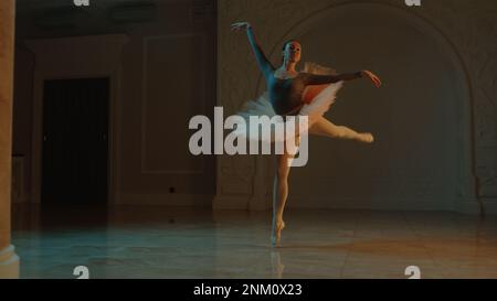 Ripresa cinematografica di una graziosa ballerina femminile durante le prove coreografiche nella hall del teatro, che praticano movimenti eleganti. Ballerina in tutu prima dello spettacolo in opera. Balletto classico teatrale Foto Stock