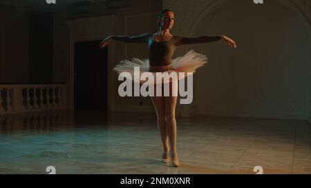 Ripresa cinematografica di una graziosa ballerina femminile durante le prove coreografiche nella hall del teatro, che praticano movimenti eleganti. Ballerina in tutu prima dello spettacolo in opera. Balletto classico teatrale Foto Stock