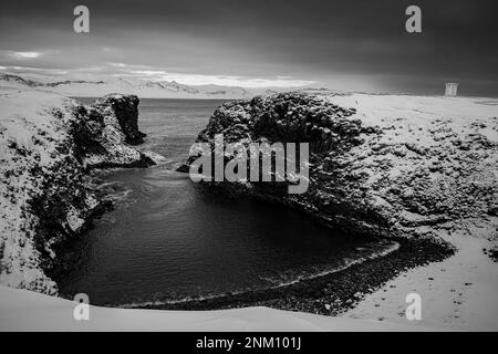 Un'immagine in scala di grigi di un lago tranquillo circondato da terreni rocciosi e innevati, con un'atmosfera misteriosa Foto Stock