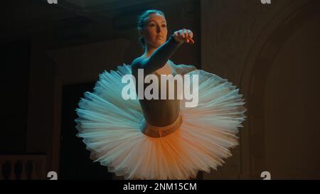 Ripresa cinematografica di una bella ballerina classica in abito tutu bianco, in piedi nella lobby del teatro e in preparazione per iniziare lo spettacolo. Stretching prima dell'inizio dello spettacolo. Balletto classico art. Foto Stock