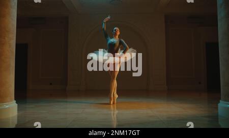 Ripresa cinematografica di una bella ballerina classica femminile in tutu bianco che balla nella lobby del teatro e si prepara ad iniziare lo spettacolo. Coreografia prima dell'inizio dello spettacolo. Balletto classico art. Foto Stock