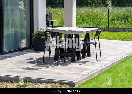 Tavolo da terrazza in pallet bianco su tralicci di plastica, sedie di plastica nera. Foto Stock