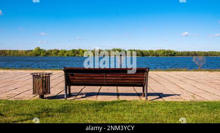 Il parco cittadino. Una panca vuota che si affaccia sulla superficie dell'acqua. Vista posteriore Foto Stock
