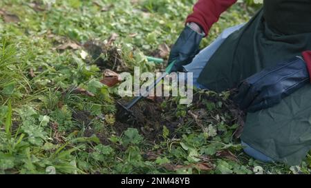 Primo piano del giovane agricoltore maschio che pettina il terreno per piantare semi di fiori o vegetali con zappa a mano, concetto di agricoltore Foto Stock