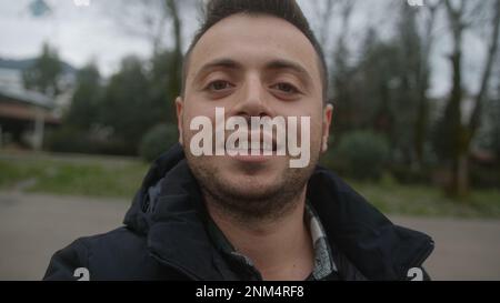 POV Selfie Video Conferenza di un bel giovane uomo dai capelli corti con pelle leale all'aperto, tenendo smartphone Foto Stock