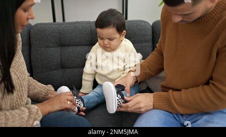 Coppia e figlio seduti sul divano che mettono le scarpe al bambino a casa Foto Stock