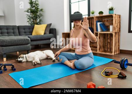 Giovane donna sorridente allenata con sicurezza utilizzando occhiali per realtà virtuale a casa Foto Stock