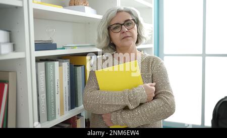 Donna di mezza età con insegnante di capelli grigi che insegna lezione di matematica che tiene un libro in classe universitaria Foto Stock