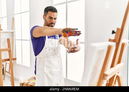 Giovane uomo ispanico che guarda tela disegnare facendo un gesto di foto con le mani in studio d'arte Foto Stock