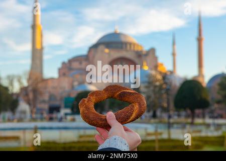 Viaggio a Istanbul foto di sfondo. Bagno turco detto Simit e Hagia Sophia. Donna che tiene un bagel o simit con mano contro la Hagia Sophia. Foto Stock