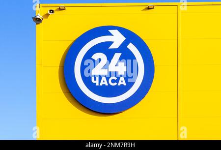24 ore blu segno aperto o di lavoro intorno al orologio appeso alla parete gialla. Negozio attivo 24 ore su 24, cartello sulla facciata dell'edificio. Iscrizione in russo: Foto Stock