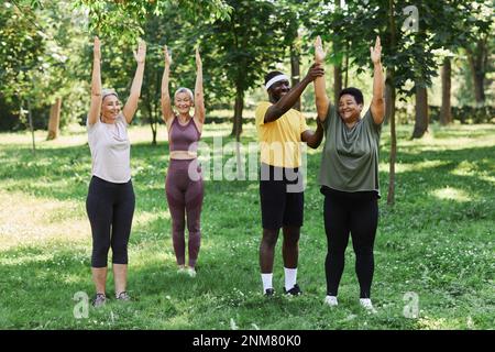 Gruppo variegato di anziani che lavorano all'aperto nel parco verde con pullman e sorridendo felicemente Foto Stock