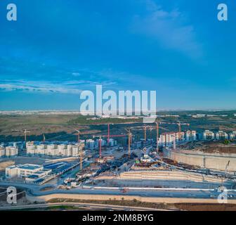 Modiin, Israele, 11 gennaio 2023. Vista aerea della costruzione di un edificio residenziale a più piani e di una grande nuova zona residenziale che si affaccia su un parco verde con alberi e un prato accanto a edifici residenziali contro un cielo blu con nuvole bianche. Foto di alta qualità Foto Stock