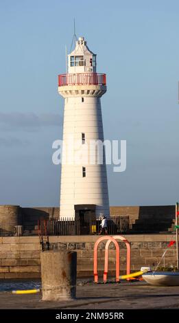 Donaghadee, County Down, Irlanda del Nord, Regno Unito. 24 Feb 2023. Tempo nel Regno Unito - un pomeriggio di sole luminoso ma un forte vento sulla costa orientale dell'Irlanda del Nord. Una donna cammina il suo cane lungo il molo di fronte al faro di Donaghadee. Credit: CAZIMB/Alamy Live News. Foto Stock