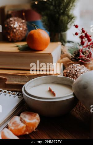 un notebook con pagine bianche accanto a libri e tangerini, candele fatte a mano. Piani e sogni per il nuovo anno Foto Stock