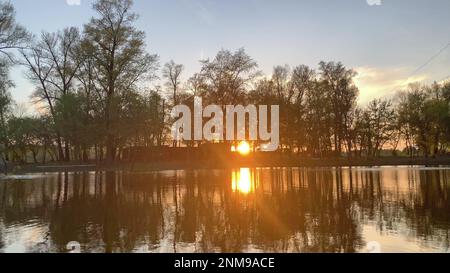 Un bellissimo tramonto sul fiume con acqua calma. Il sole splende attraverso gli alberi Foto Stock