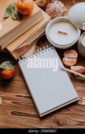 un notebook con pagine bianche accanto a libri e tangerini, candele fatte a mano. Piani e sogni per il nuovo anno Foto Stock