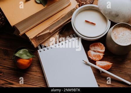 un notebook con pagine bianche accanto a libri e tangerini, candele fatte a mano. Piani e sogni per il nuovo anno Foto Stock