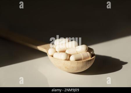 Pillole in un cucchiaio di legno su un tavolo al sole, medicine e vitamine Foto Stock