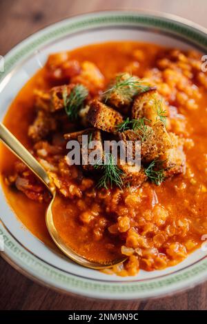 zuppa di lenticchie rosse e pomodoro con finocchio e crostini in recipiente bianco con chiave greca verde e cucchiaio d'oro Foto Stock