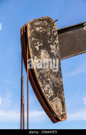 Primo piano di una testa di cavallo arrugginita grunga di un pozzo di petrolio con briglia o wireline - cavi- contro il cielo blu Foto Stock