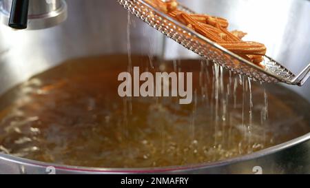 Preparare i churros fritti. Street food fornitore prepara churros all'interno di una grande padella oleosa. Piatti tradizionali spagnoli del Churro Foto Stock