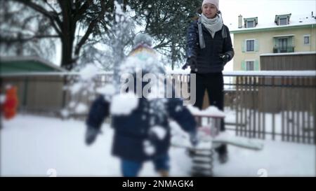 Madre che lancia la palla di neve al bambino. Genitori e bambini che giocano con la neve. La mamma lancia la battaglia della palla di neve Foto Stock