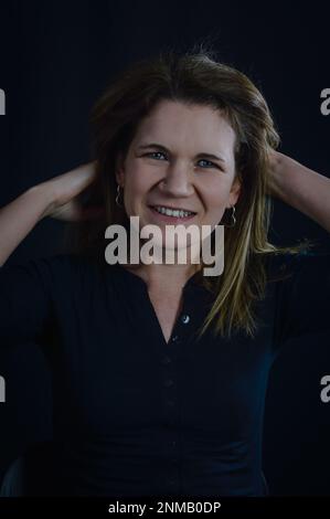 ritratto di una bella donna bionda che tiene i capelli dietro la testa e sorride in modo amichevole Foto Stock