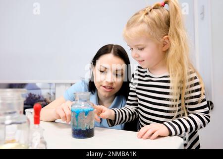 Scuola elementare Scienza chimica Classroom: Entusiasta insegnante mostra Funny Chemical Reaction Experiment a diversi gruppi di bambini. Miscelazione di prodotti chimici nel becher per sparare la schiuma Foto Stock