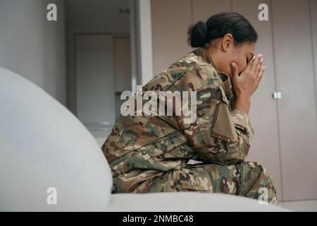 Una soldato afro-americana stanca si siede da sola in una stanza luminosa Foto Stock