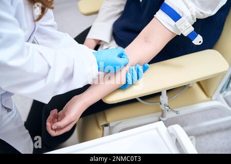 L'assistente di laboratorio inserisce un ago nella vena del paziente Foto Stock