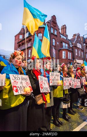 Donna con corone floreali in possesso di 365 giorni di guerra sofferenza cartelloni al 'heartbroken ma unbroken', ricordo evento che segna l'anniversario di R Foto Stock