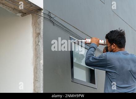 Addetto alla messa in primo piano che installa le finestre con silicone a pistola in cantiere. Foto Stock