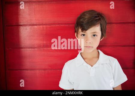 Sentirsi blu oggi. Ritratto di un ragazzino triste in piedi contro un muro rosso. Foto Stock