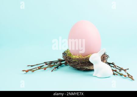 Coniglietto di Pasqua o coniglio seduto accanto a un nido di vimini pieno di uovo colorato, vacanze primaverili Foto Stock