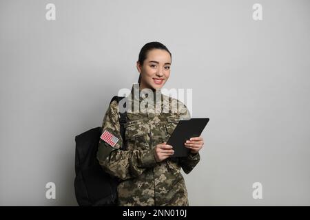 Soldato femminile con tablet e zaino su sfondo grigio chiaro. Educazione militare Foto Stock