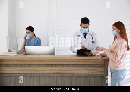 La receptionist parla al telefono mentre il medico lavora con il paziente in ospedale Foto Stock