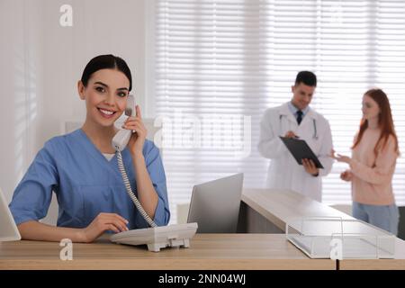 La receptionist parla al telefono mentre il medico lavora con il paziente in ospedale Foto Stock