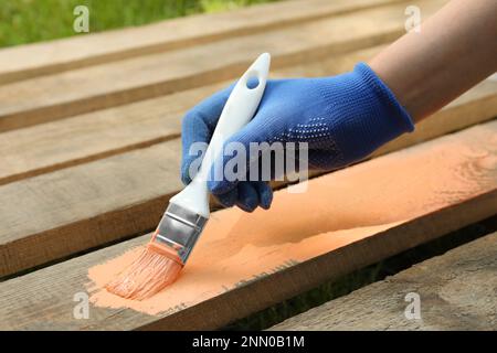 Donna che dipinge la superficie di legno con la tintura di corallo all'aperto, primo piano Foto Stock