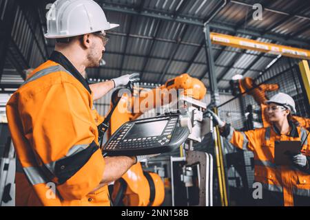 Team di tecnici addetti alla manutenzione della saldatura robotizzata che lavora nello stabilimento di automazione. Le persone che lavorano in tuta di sicurezza lavorano la programmazione o la sostituzione del software del braccio robotico par Foto Stock