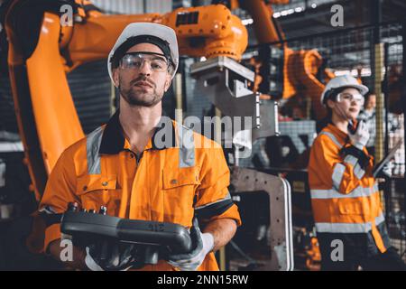 Team di tecnici addetti alla manutenzione della saldatura robotizzata che lavora nello stabilimento di automazione. Le persone che lavorano in tuta di sicurezza lavorano la programmazione o la sostituzione del software del braccio robotico par Foto Stock