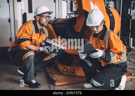 Team di tecnici addetti alla manutenzione della saldatura robotizzata che lavora nello stabilimento di automazione. Le persone che lavorano in tuta di sicurezza lavorano la programmazione o la sostituzione del software del braccio robotico par Foto Stock